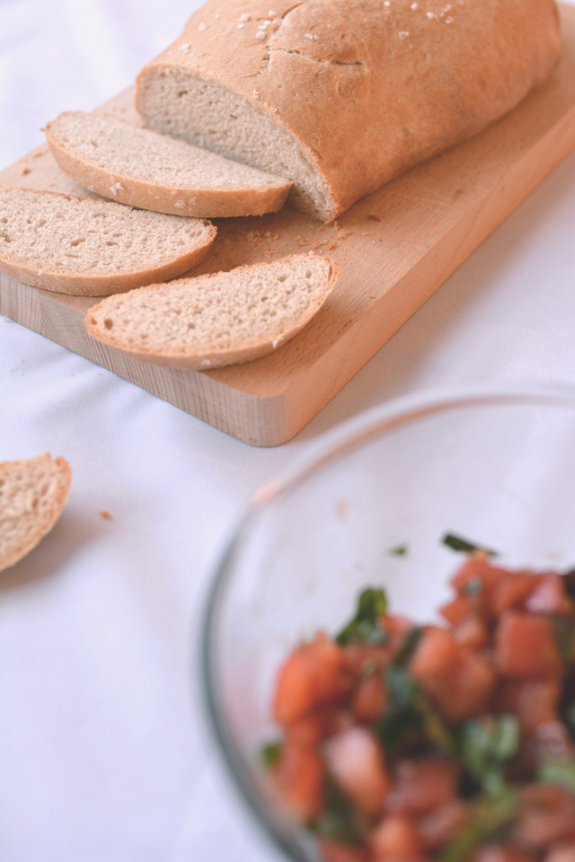 Slices for homemade olive oil bread on a cutting board with tomato and basil topping in a bowl.