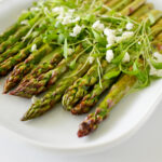 close up view image of asparagus stem topped with fresh parsley and coriander, drizzled with dressing