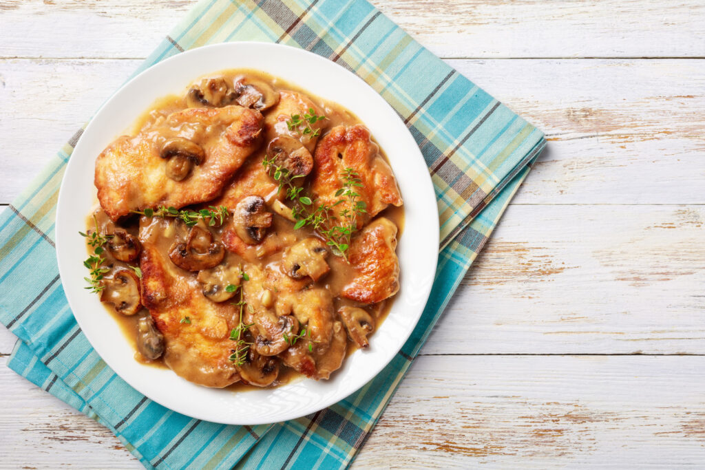 Healthy chicken and mushrooms on a white plate on a rustic table.