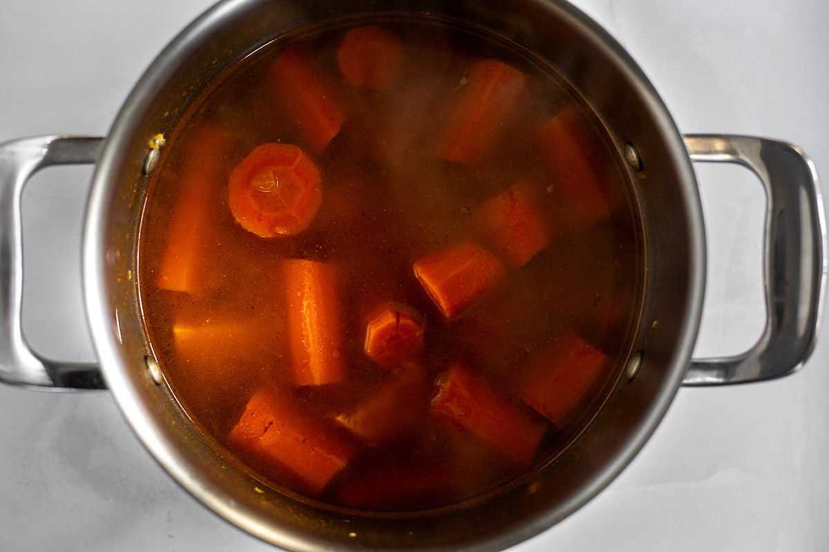 A soup pot filled with carrots and sweet potatoes that are simmering. 