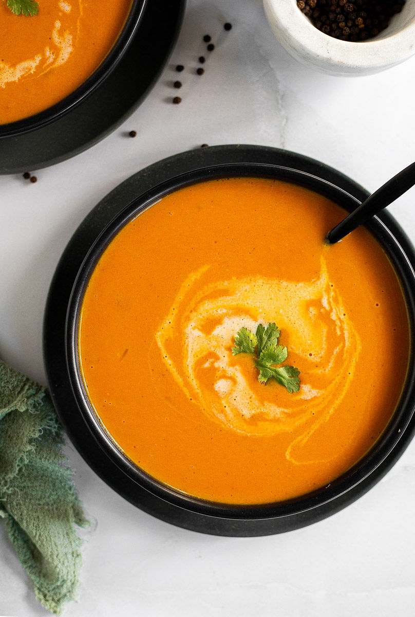 A black soup bowl with coconut carrot soup, garnished with cilantro, and a spoon.