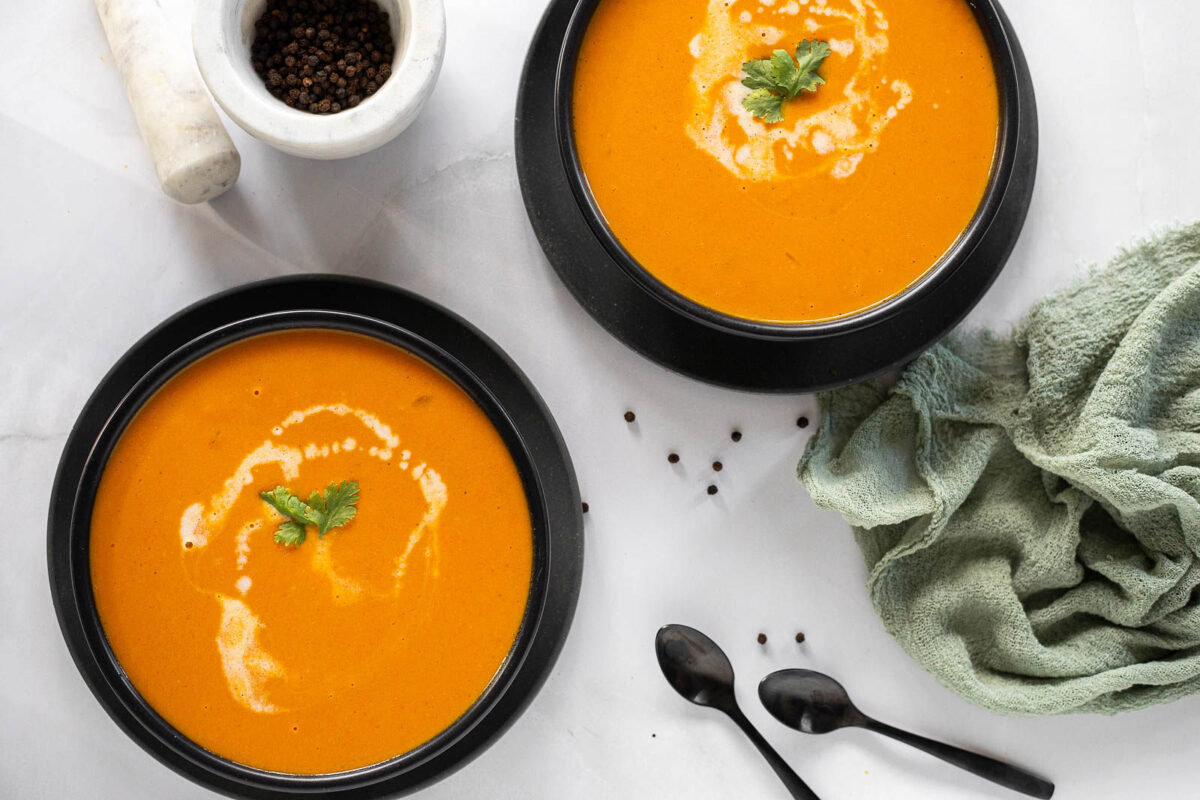 Two bowls of coconut carrot soup with two spoons and a green napkin.