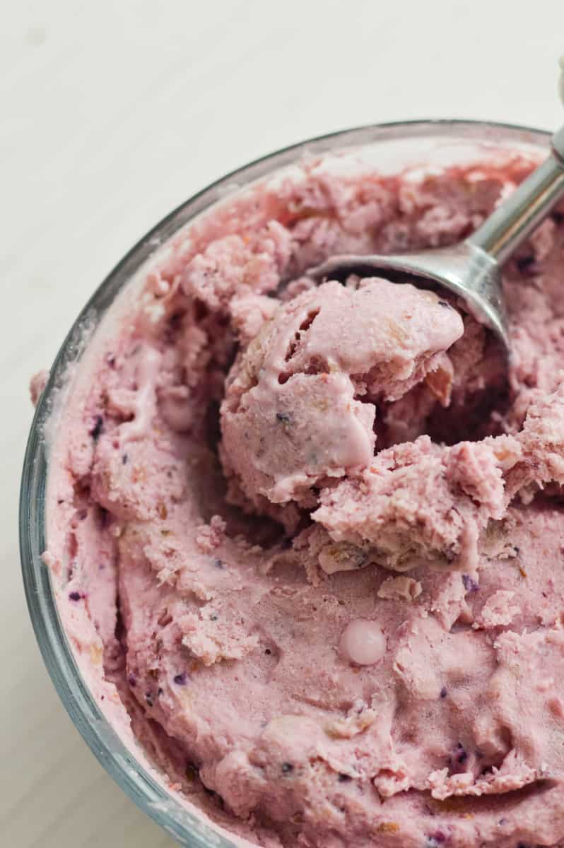 Berry flavored cottage cheese ice cream being scooped from a glass bowl.