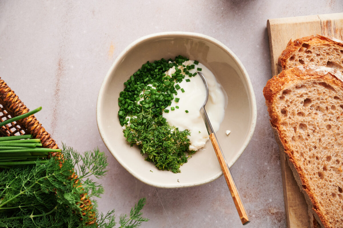 Ingredients for cucumber sandwich spread in a bowl, including dill, chives, light cream cheese, and Greek yogurt.