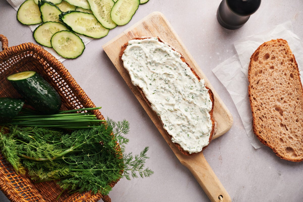 Creamy herb spread smeared on a piece of bread on a cutting board.