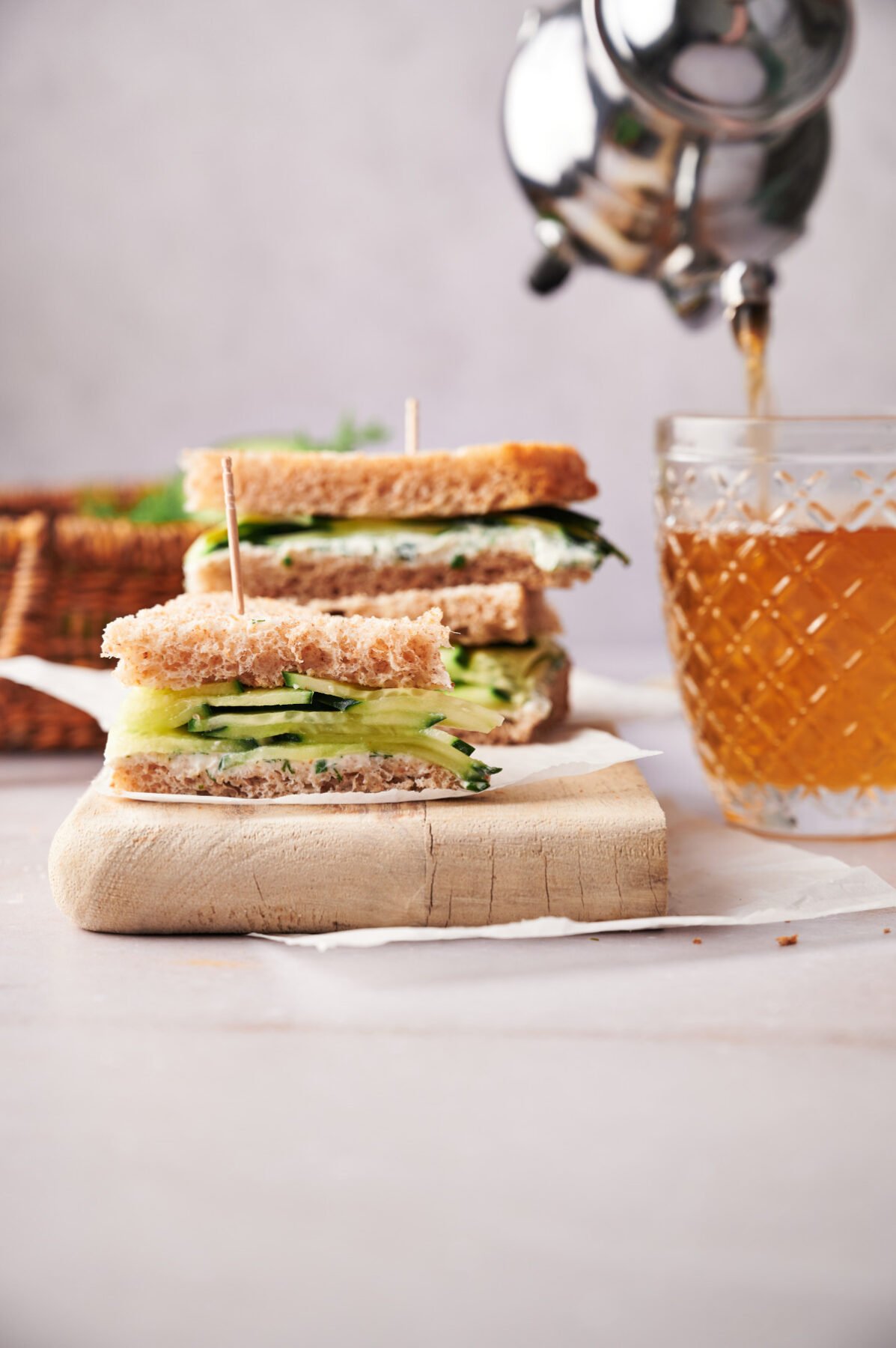 Small cucumber sandwich appetizers with tea being poured in the background.