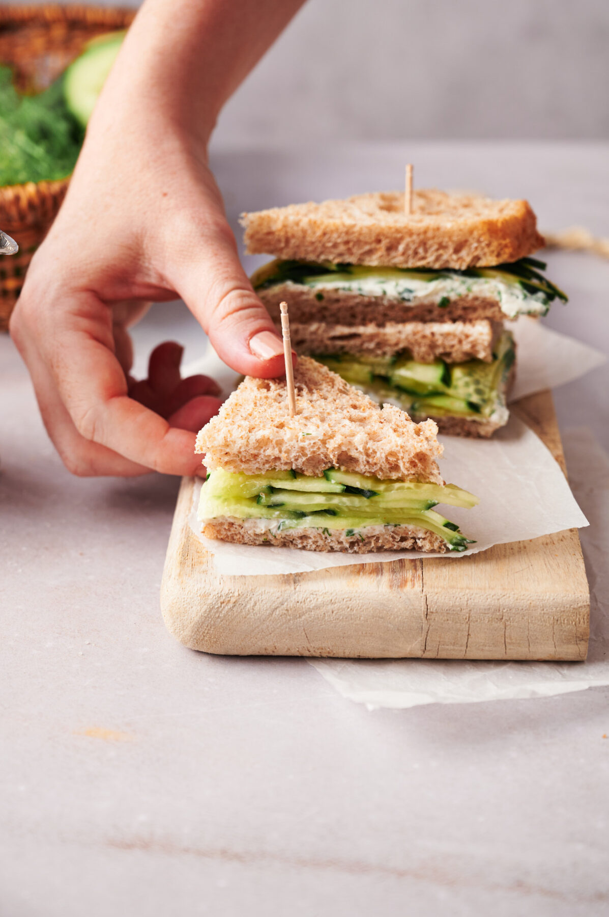 Small cucumber sandwich cut into a triangle shape on a cutting board.