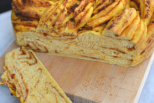 cropped image of a freshly baked sweet potato and sun-dried tomato braided bread resting on a cutting board, with two slices cut from it