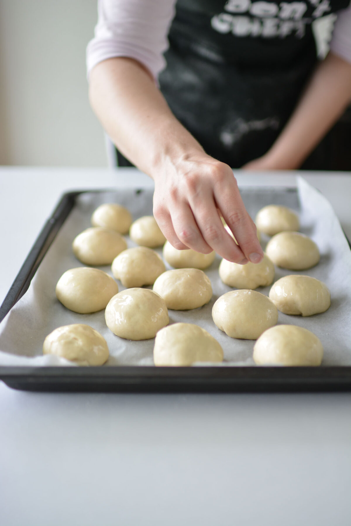 A woman skillfully shaping dough balls on a baking tray in preparation for baking.