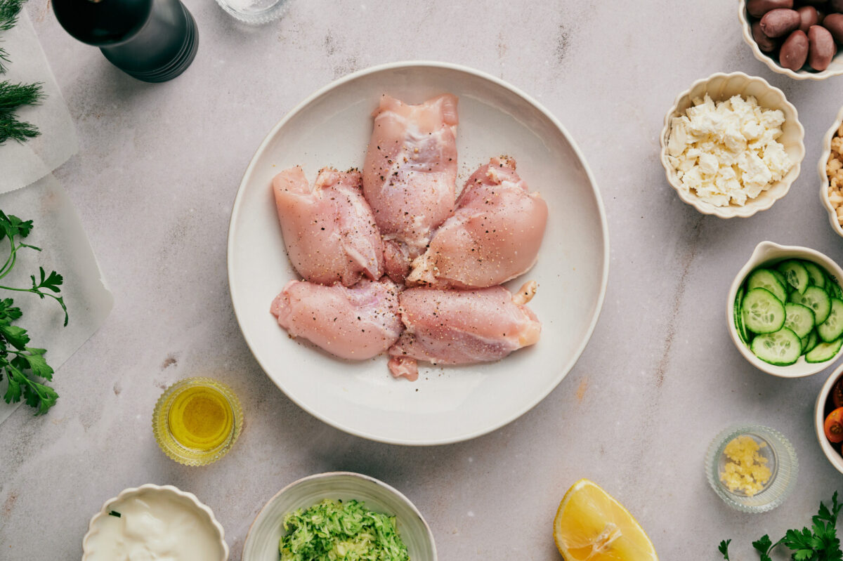 Chicken thighs on a white plate seasoned with salt and pepper.