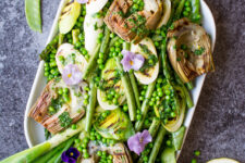 top down cropped photo of a serving dish containing grilled spring vegetables including french green beans, spring onions, sugar snap peas, asparagus, leeks, and artichokes, glisten with a homemade lemon parsley butter