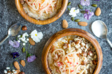 Top-down view of a 2 wooden bowl containing creamy oatmeal adorned with grated apple, toasted hazelnuts, and a sprinkle of sweet brown sugar.