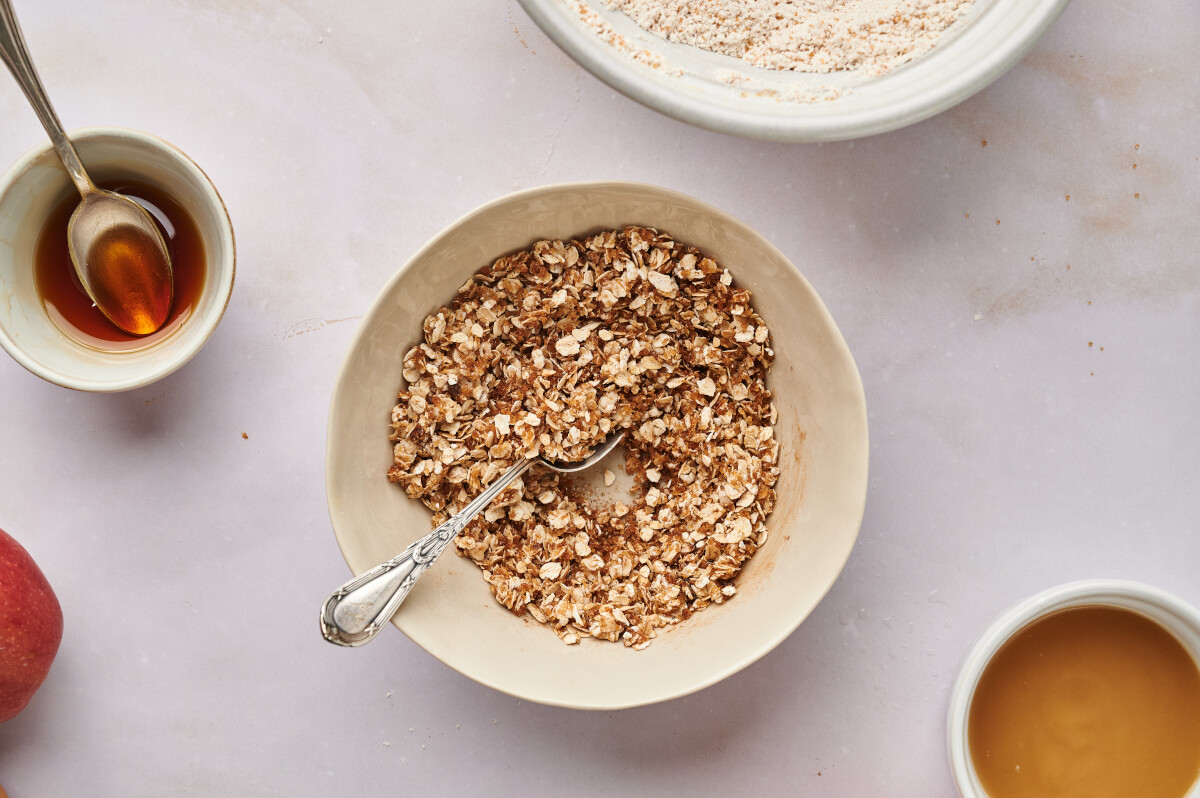 Ingredients for crumble mixture for healthy apple bread. A bowl of oats with brown sugar and a spoon and other bowls filled with ingredients.