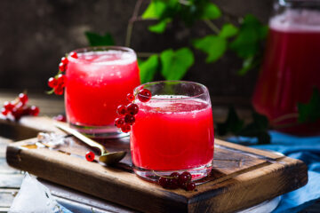 Homemade red kombucha in two glasses on a cutting board.