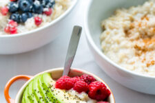 a cropped image of a bowl containing an oatmeal topped with fresh slices of avocado and raspberries