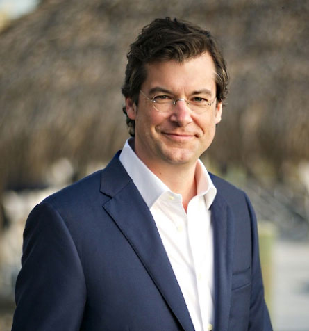 A man with short brown hair, glasses, a white shirt and dark jacket. 