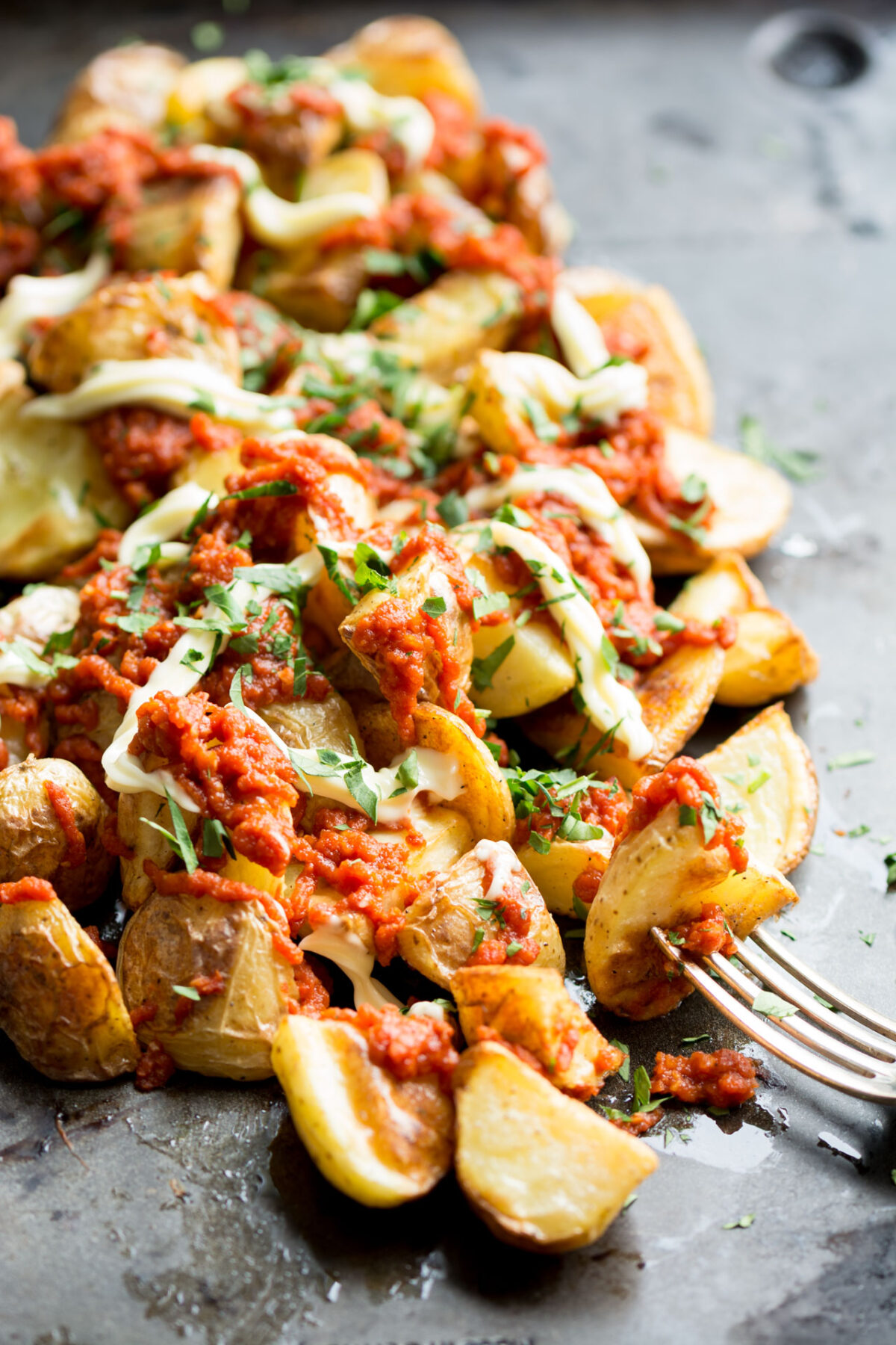 Patatas bravas close up on a griddle top with a fork in the foreground.