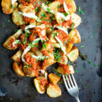 Seasoned patatas bravas on a griddle top covered in tomato sauce with a fork.