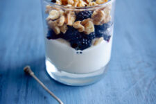 A parfait with granola and a metal spoon beside it.