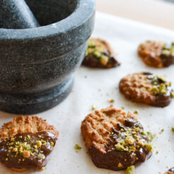 cropped image of Flourless Peanut Butter, Chocolate and Pistachio Cookies flourless peanut butter, chocolate, and pistachio cookies arranged flat on parchment paper, with a stone and mortar and pestle beside them