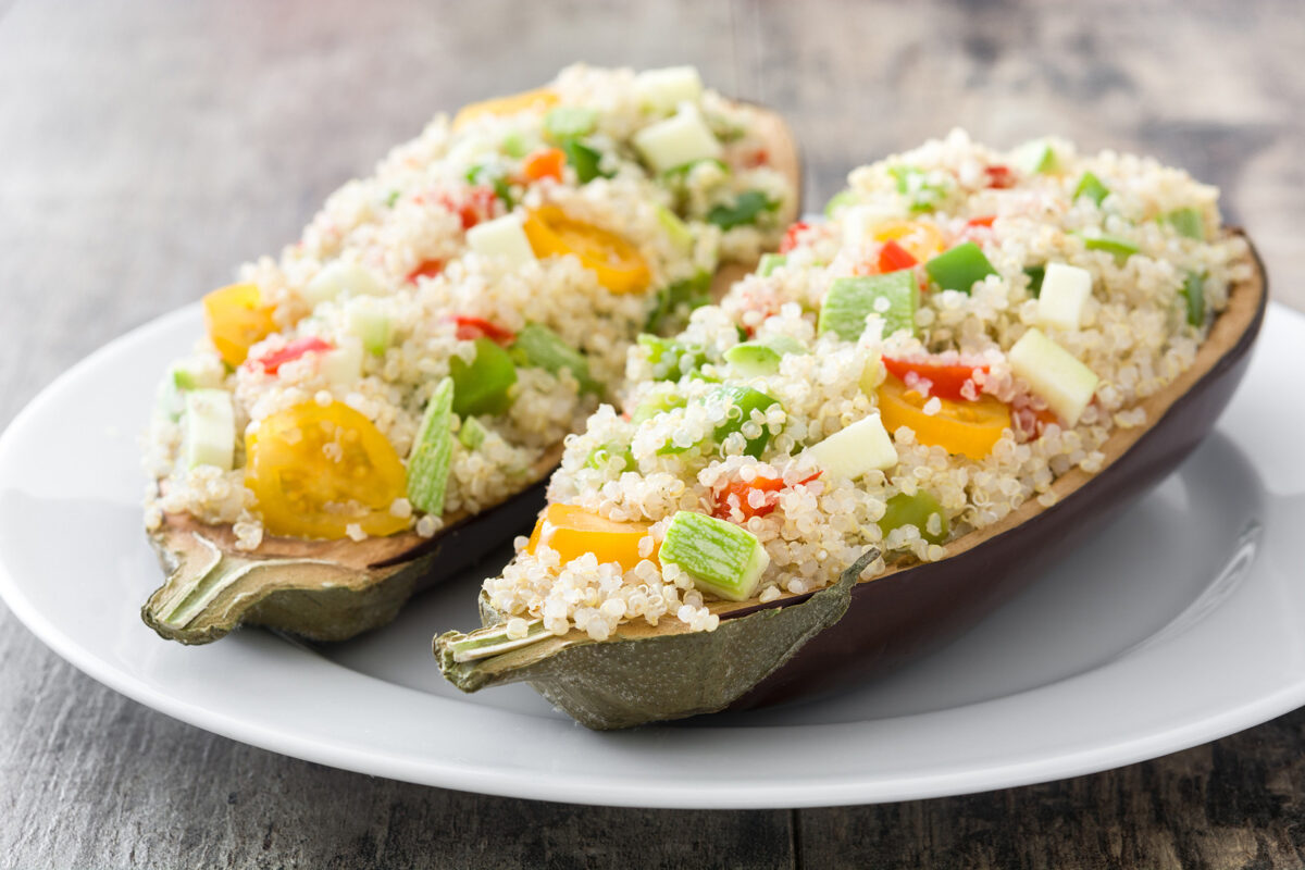 Stuffed eggplant with quinoa and vegetables on a white plate on a wooden table.