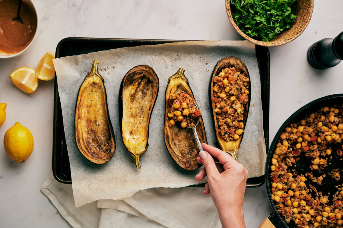 Adding chickpea and quinoa filling to roasted eggplants on a baking sheet with parchment paper.