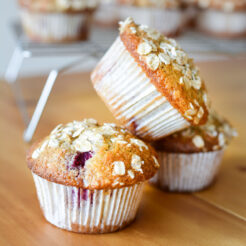 A stack of three delicious raspberry and coconut muffins, topped with oats, showcasing their golden-brown texture and enticing appearance