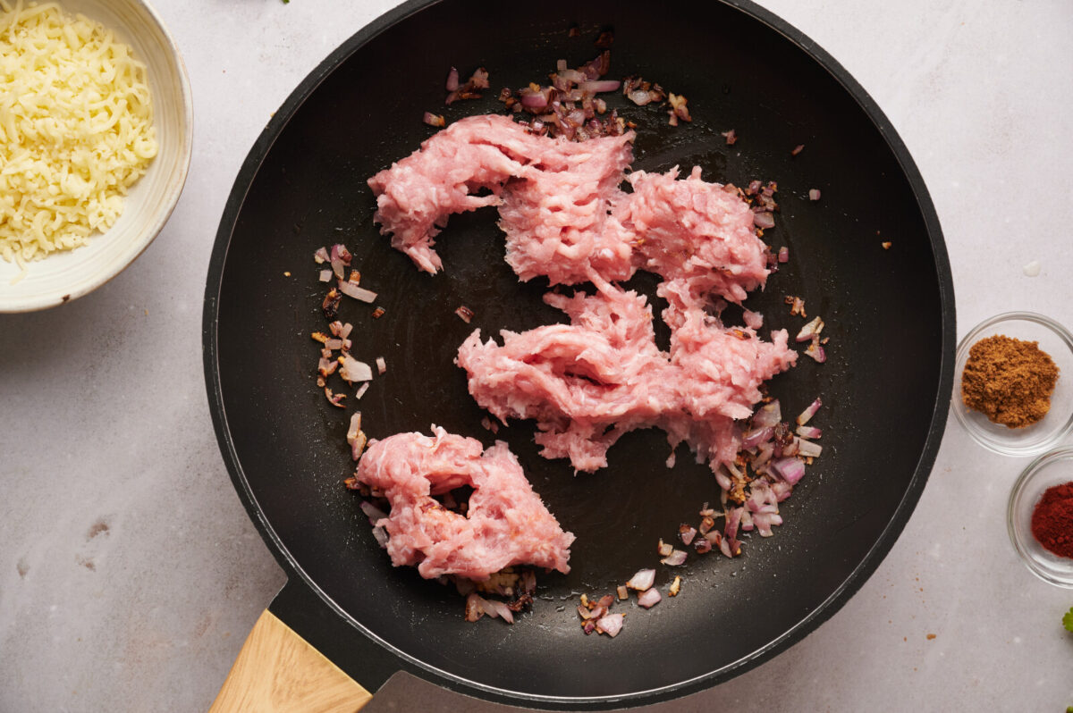 Ground turkey being sautéed in a skillet with onion and garlic.