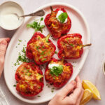 Southwestern stuffed peppers served with sour cream and cilantro on a platter with hands holding it.