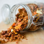 cropped image of a glass canister lying on its side, filled with a mixture of overflowing rolled oats and whole almonds