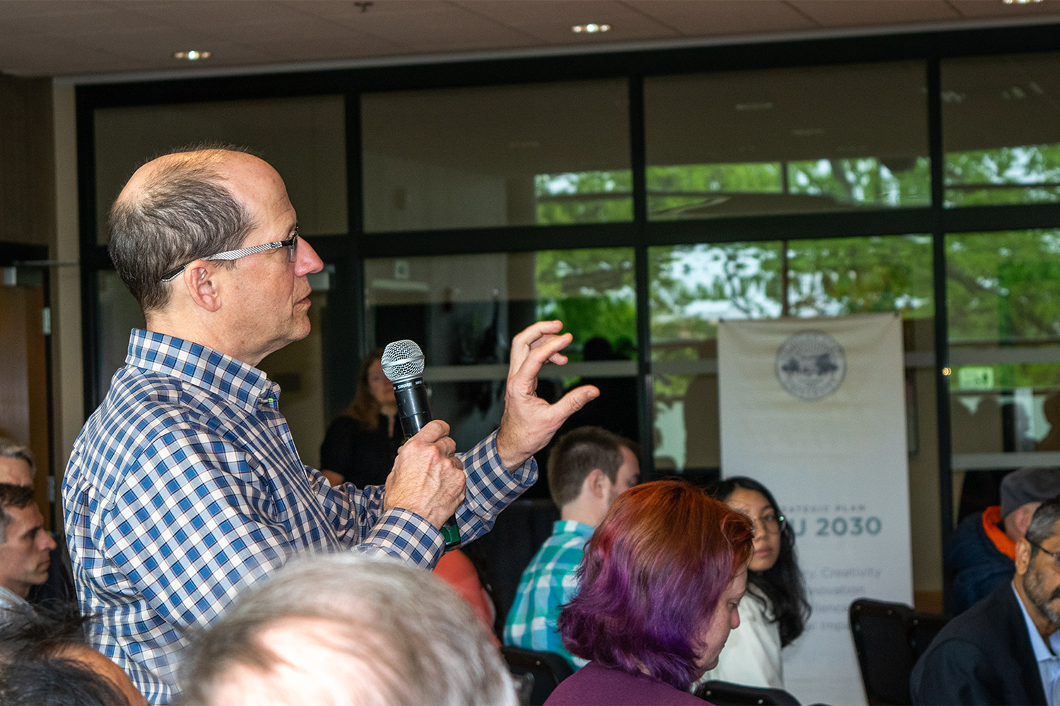 A person holding a microphone, standing in the audience of an event.