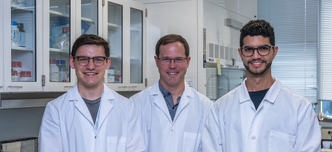 Three members of a lab wearing white coats stand for a picture