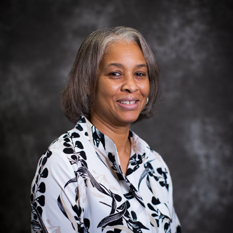 A woman with shoulder-length grey hair, and a blouse with a black and white pattern.