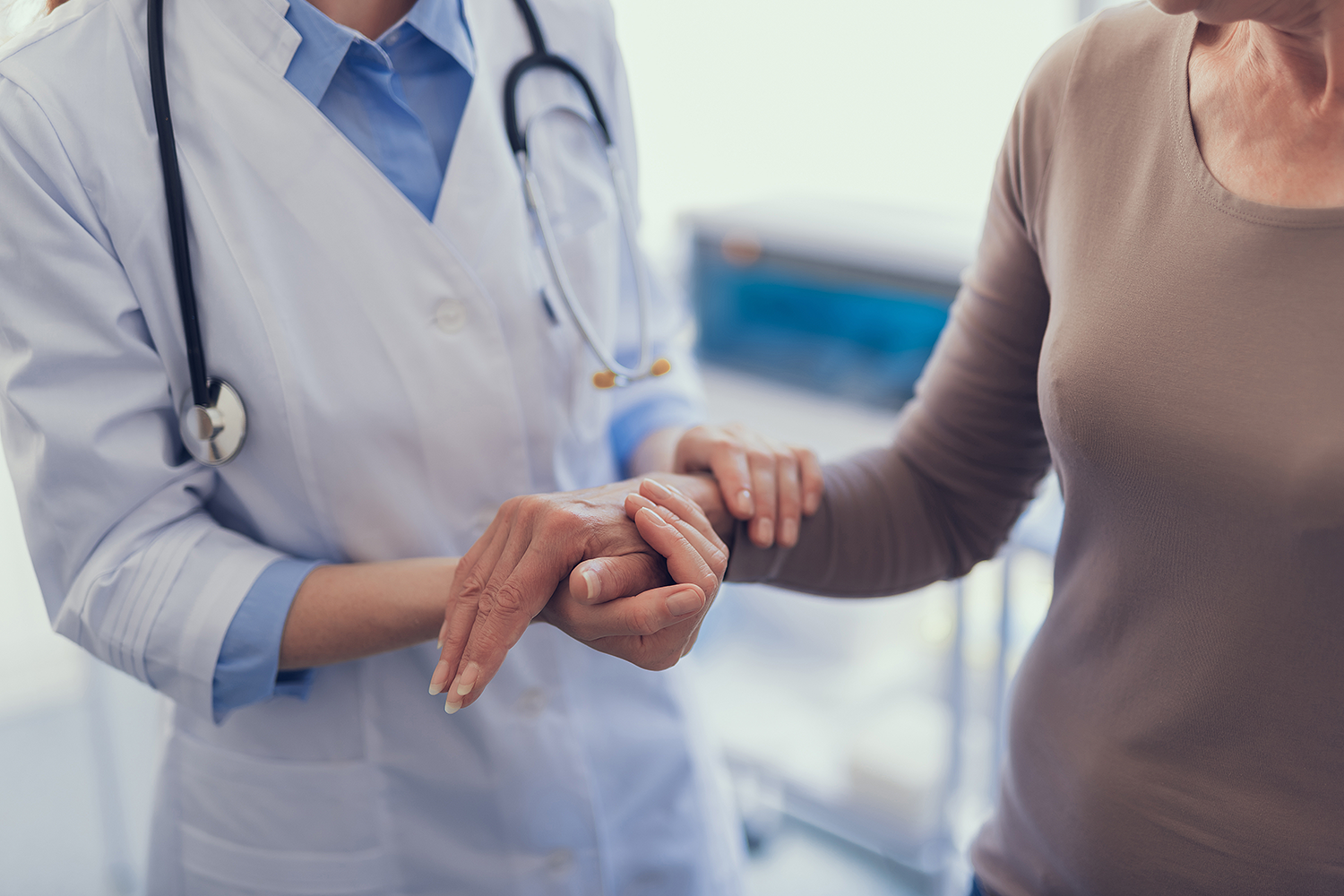 A doctor in a white lab coat holds the hand and arm of a patient.