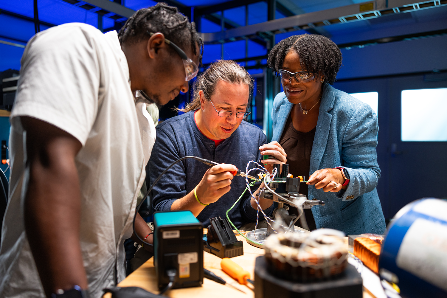 Three people standing at a table and interacting with various machines. 