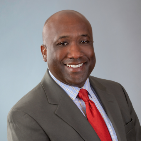 A man wearing a red tie, blue checkered shirt, and grey jacket