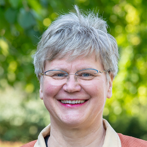 A woman with short grey hair, glasses, standing outside