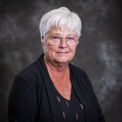 A woman with short, white hair, glasses, and a dark blouse. 